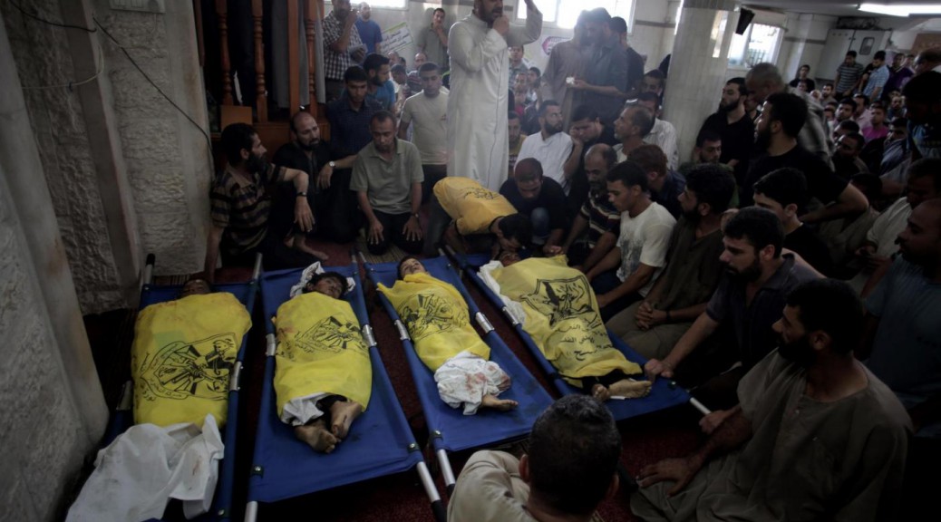 Palestinians mourn over the lifeless bodies of four boys from the same extended Bakr family, covered with yellow flags of Fatah movement, in the mosque during their funeral in Gaza City, Wednesday, July 16, 2014.  The four boys, who were cousins and ages 9 to 11, were killed while playing on a beach off a coastal road west of Gaza City, said Ashraf Al Kedra, a Palestinian doctor. Seven others _ adults and children _ were wounded in the strike, he said. (AP Photo/Khalil Hamra)