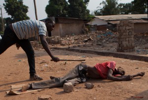 FILE - In this Tuesday, Dec. 31, 2013 file photo, a member of an armed neighborhood defense squad, which residents say is not anti-balaka but local Christian men protecting themselves, strikes the body of a man said to be Muslim with the side of a machete heated in the fire, in Bangui, Central African Republic. The interim leader of Central African Republic is vowing that the era of anarchy in the tumultuous country is now over. It's a bold declaration just days after rebel leader-turned-president Michel Djotodia agreed to step down and went into exile in Benin. (AP Photo/Rebecca Blackwell, File)